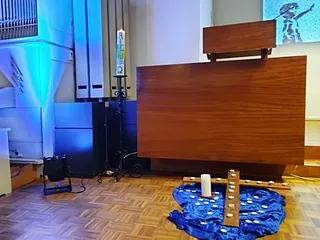 Foto von Teelichtern auf einem Kreuz und einem Tuch mit der Kanzel der Lichtenplatzer Kapelle im Hintergrund